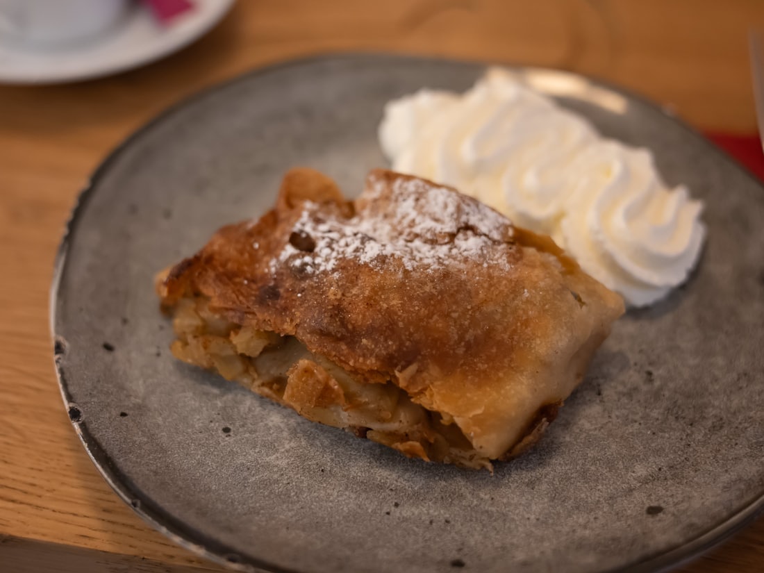 Portion Apfelstrudel mit Staubzucker und Schlagobers auf einem Steingutteller