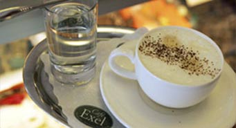 Melange mit Wasserglas auf einem Silbertablett, die Untertasse trägt das Logo des Café Exel