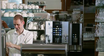 Blick hinter die Theke des Café Exel auf Kaffeemaschine und Tassenregal