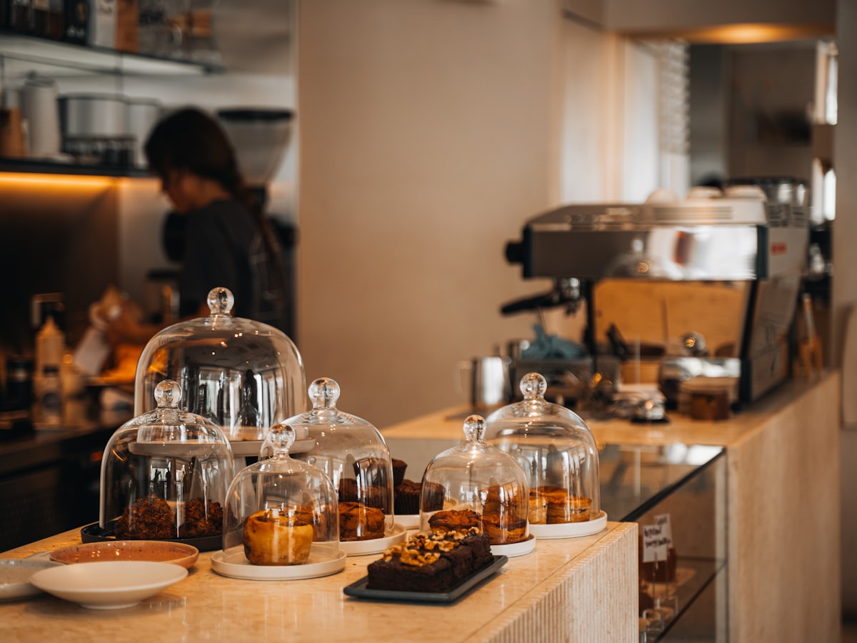 Cafétresen mit Gebäck unter Glasglocken und Espressomaschine im Hintergrund